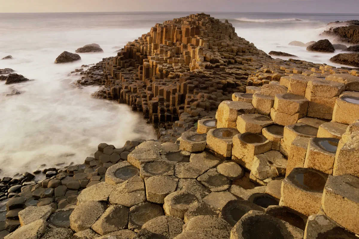 Two people walking along the Giant's Causeway with green hills behind