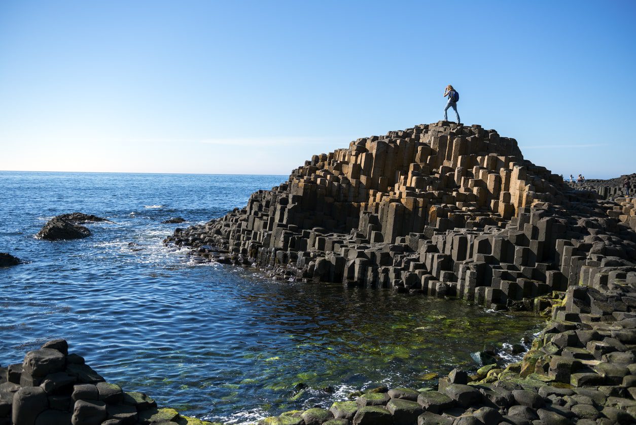 Giant's Causeway basalt columns stretching to green mountain under blue sky
